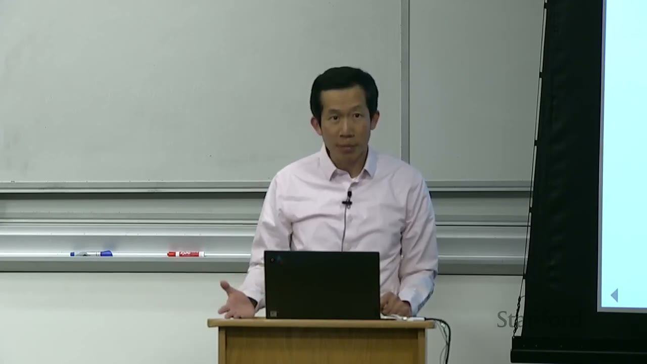 Professor presenting, gesturing with his right hand, looking at the audience.