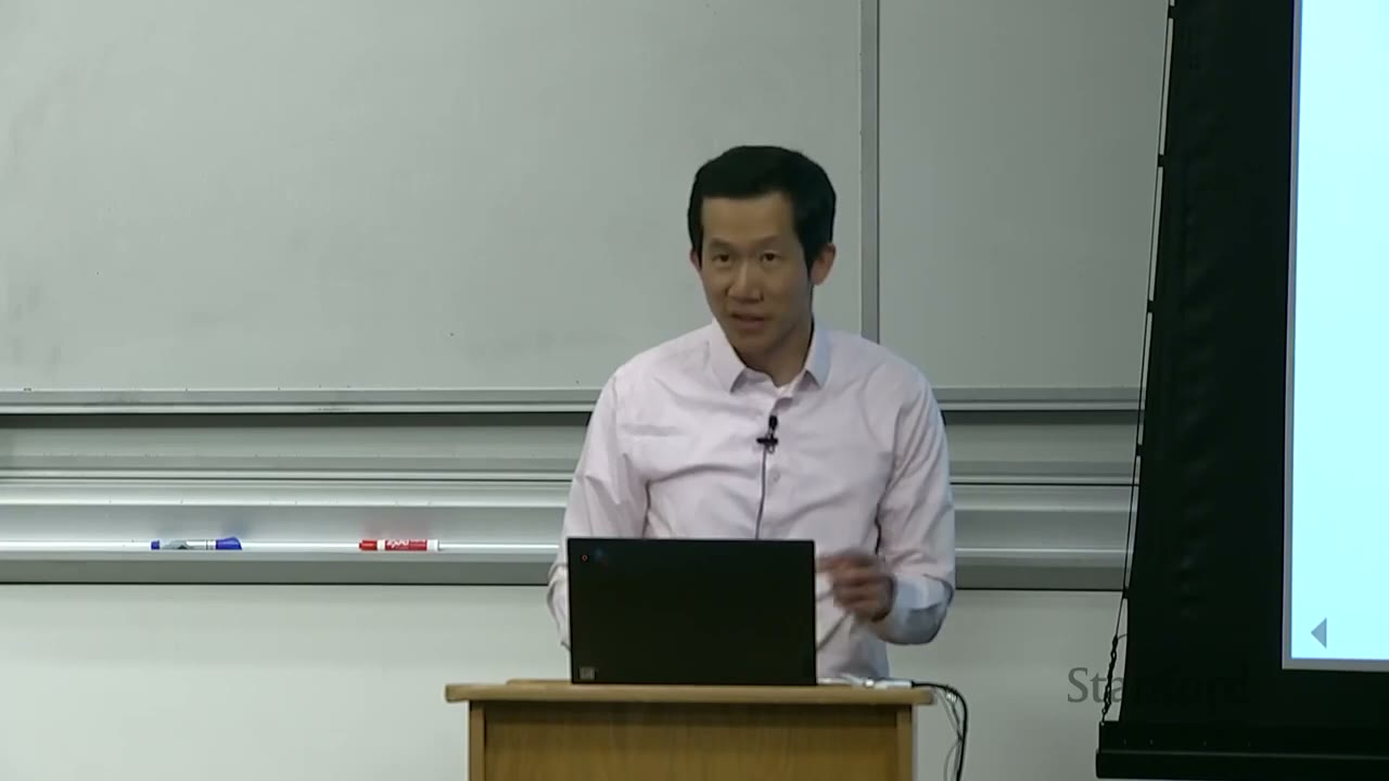 Professor looking up from his laptop, speaking to the audience.